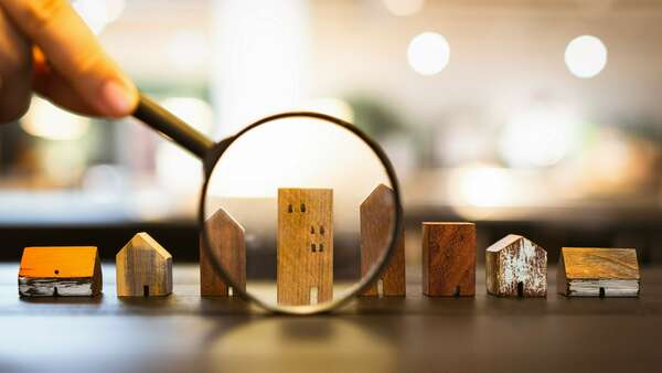 Hand holding magnifying glass and looking at house model